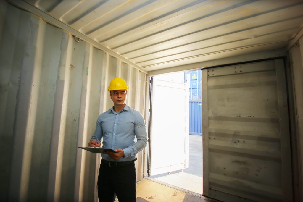 Foreman wearing hard hat holding clipboard standing inside shipping Container box for onsite business or construction storage
