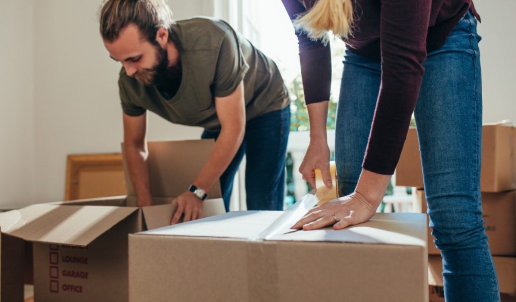 man assembling packing box beside woman sealing box with tape