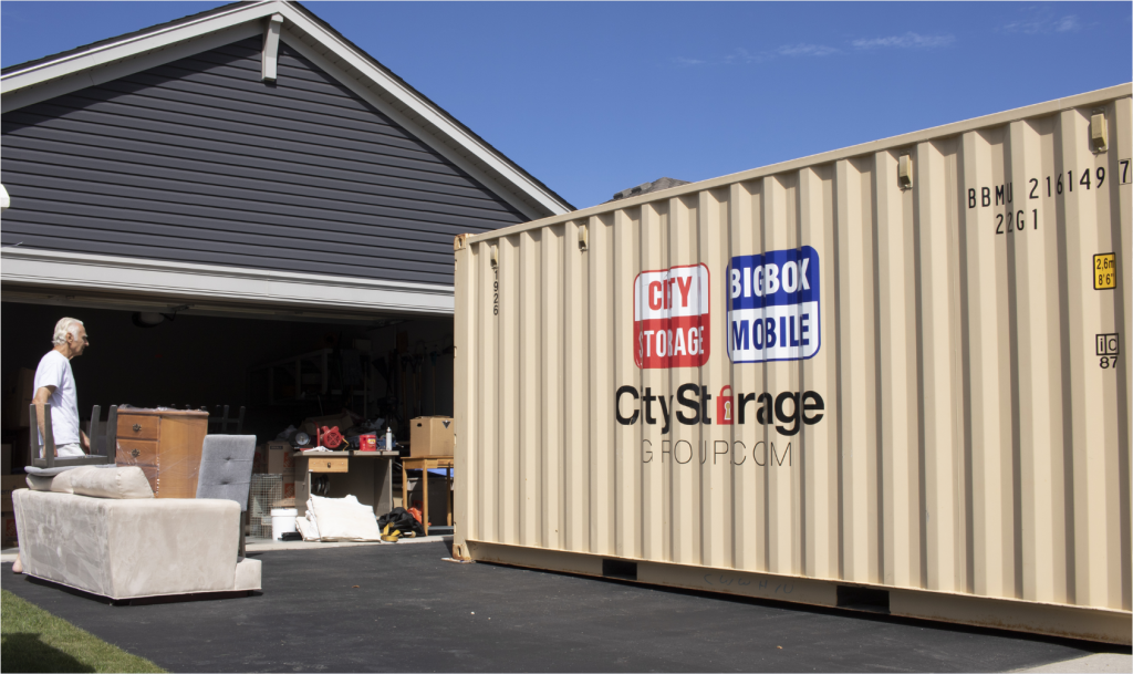 shipping-box-ground-level in residential driveway in front of open garage with man preparing to load furniture in the shipping bin